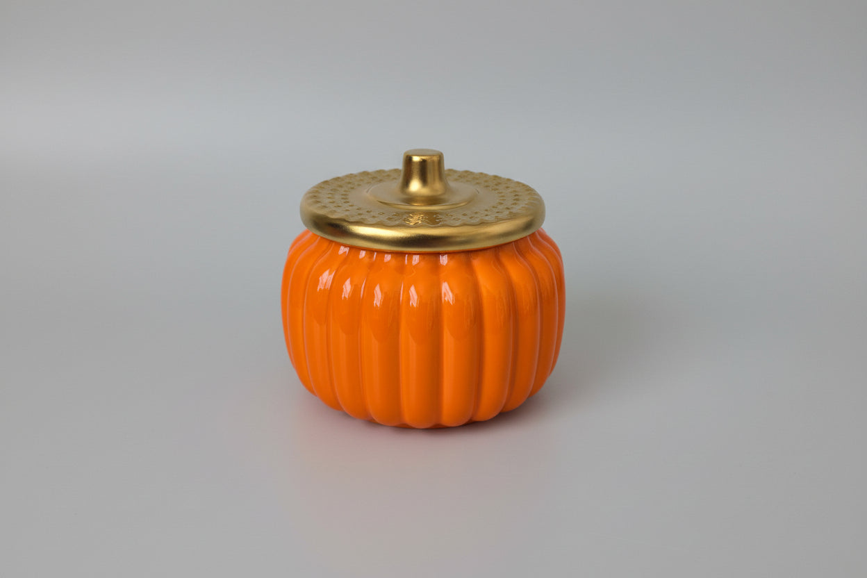 Orange pumpkin-shaped container with a gold lid on a white surface