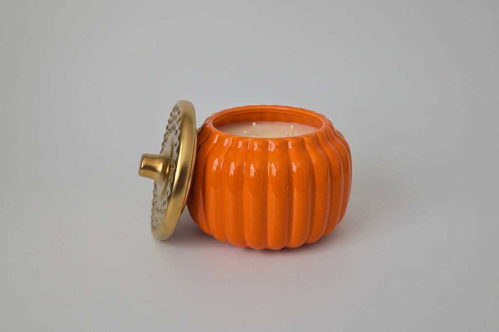 Orange pumpkin-shaped candle with a gold lid on a white surface
