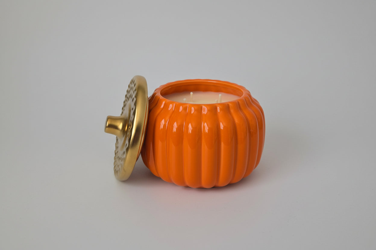 Orange pumpkin-shaped candle with a gold lid on a white surface