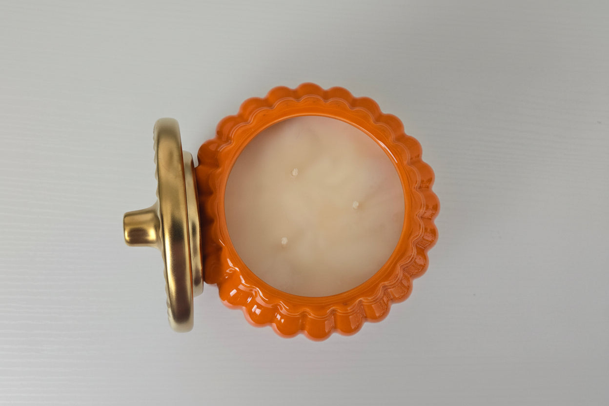 Decorative candle with an orange scalloped lid on a white background