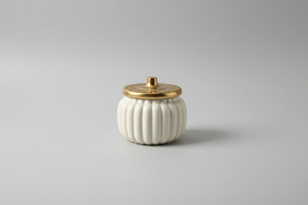 White pumpkin-shaped container with a gold lid on a white surface.