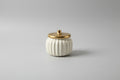 White pumpkin-shaped container with a gold lid on a white surface.