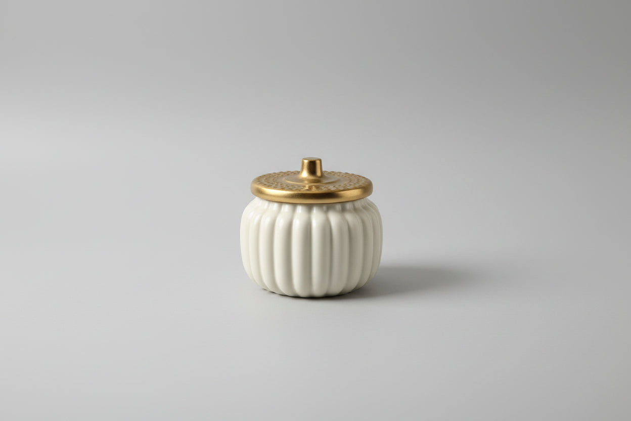 White pumpkin-shaped container with a gold lid on a white surface.