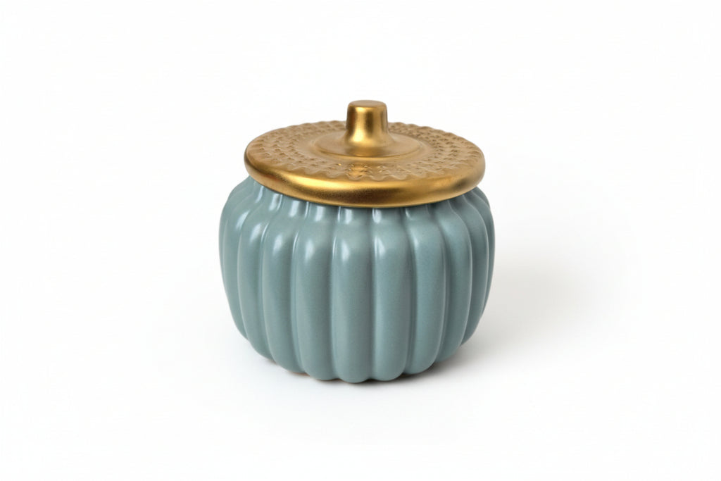 Ceramic pumpkin-shaped container with a gold lid on a white surface