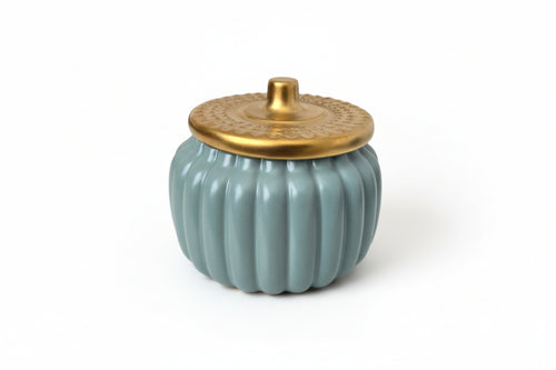 Ceramic pumpkin-shaped container with a gold lid on a white surface