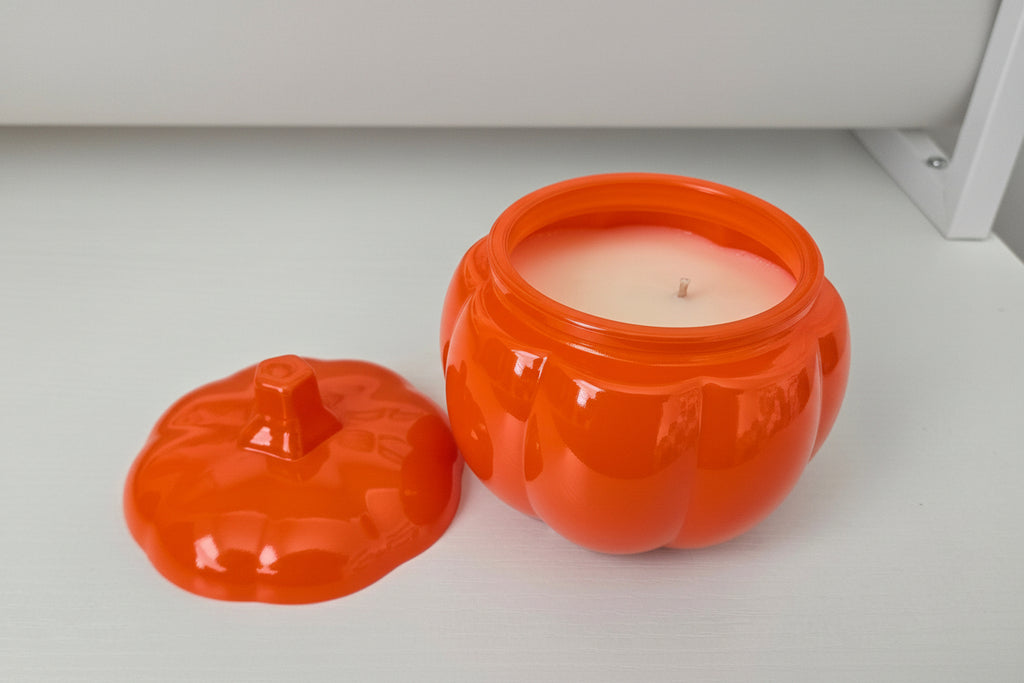 Orange pumpkin-shaped container with a candle inside on a white surface