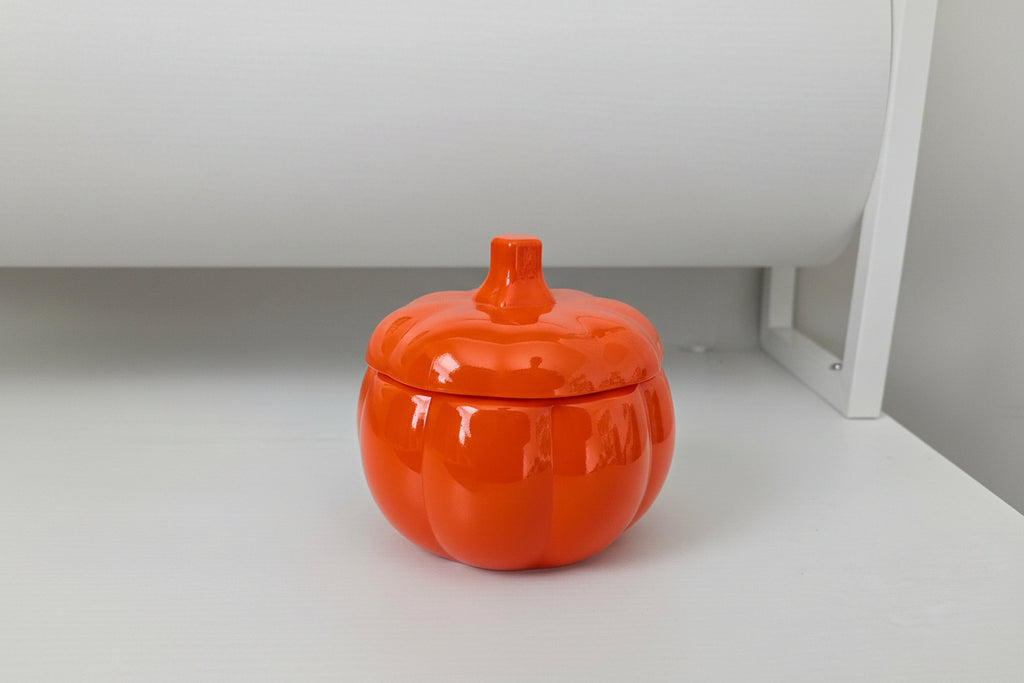 Orange ceramic pumpkin-shaped container on a white surface