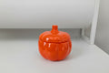 Orange ceramic pumpkin-shaped container on a white surface