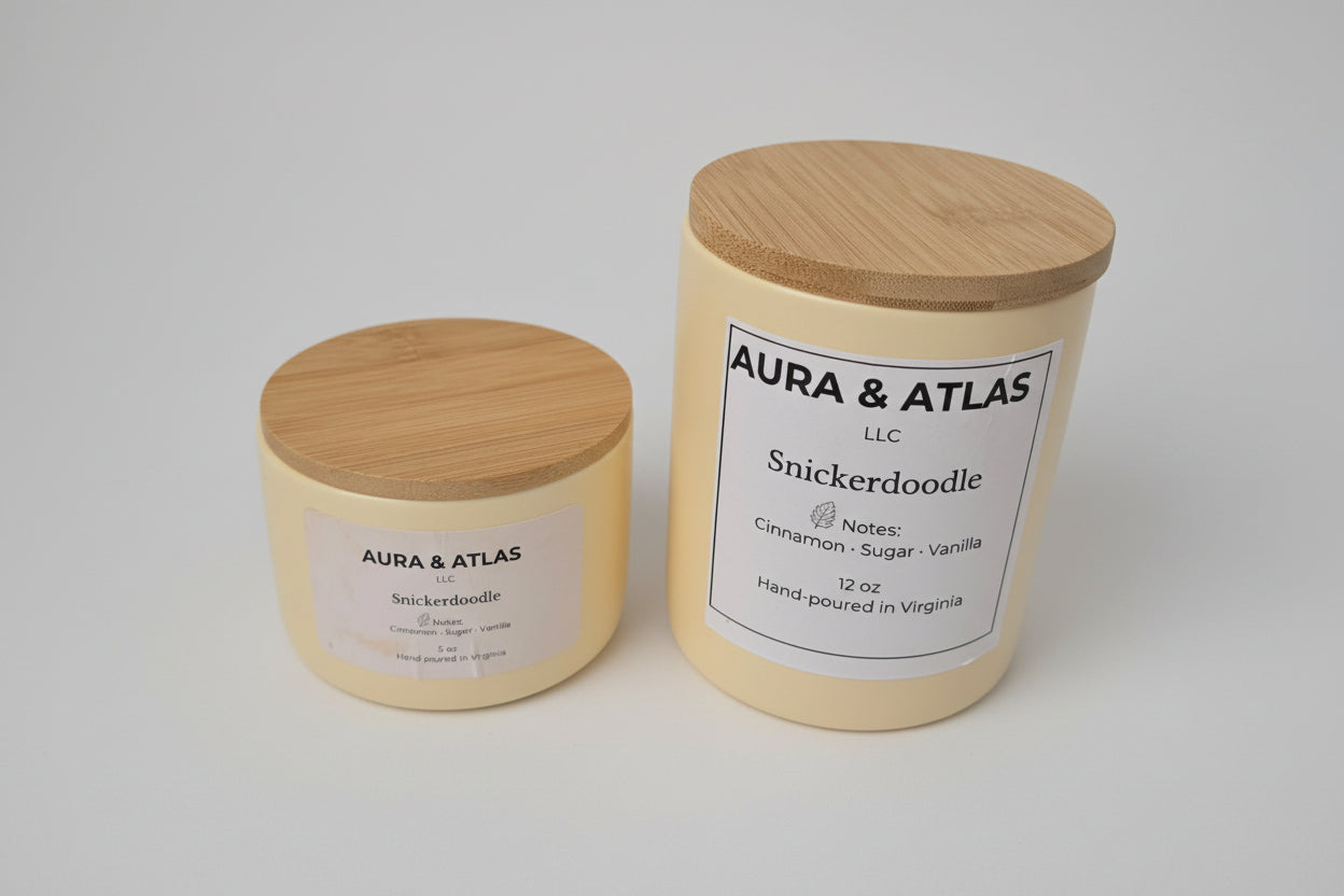 Two candles with wooden lids on a white surface, one labeled 'Aura & Atlas' and the other 'Snickerdoodle'.