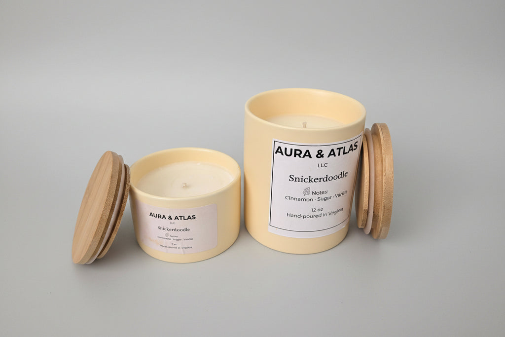 Two candles with wooden lids on a white surface, branded 'Aura & Atlas'.