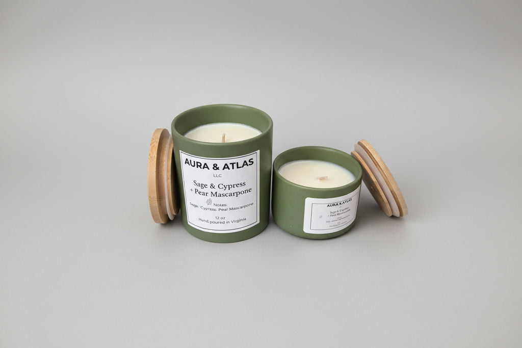 Two green candles with wooden lids on a white surface, featuring 'Aura & Atlas' branding.