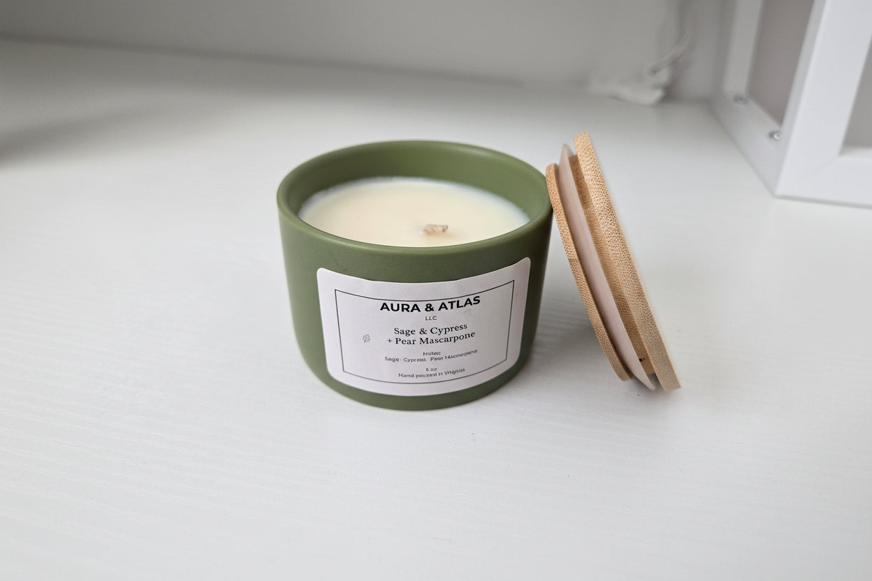 Candle in a green container with a wooden lid on a white surface, featuring 'AURA & ATLAS' branding.
