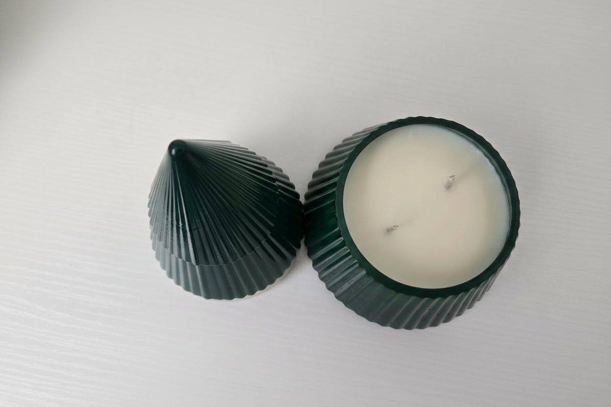 Green shell-shaped candle holder with a white candle inside on a white background
