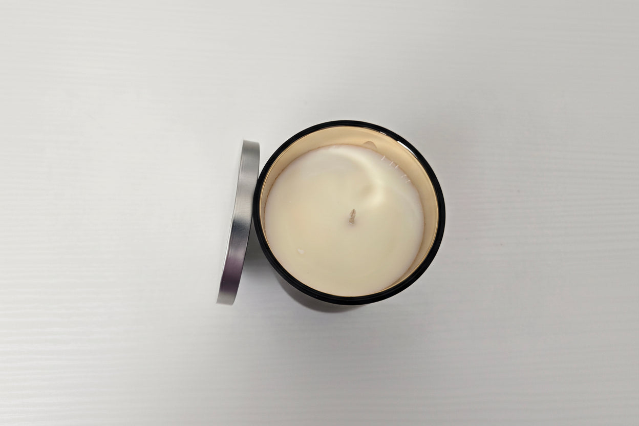 White candle in a black container with a silver lid on a light gray background
