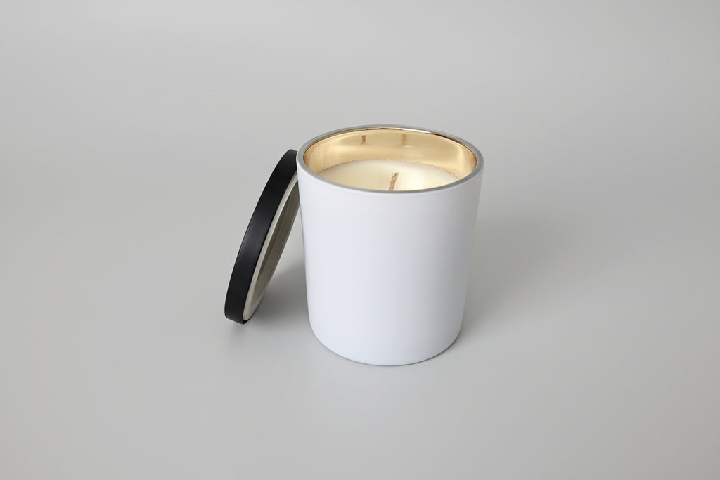 Candle in a gray container with a black lid on a light gray surface