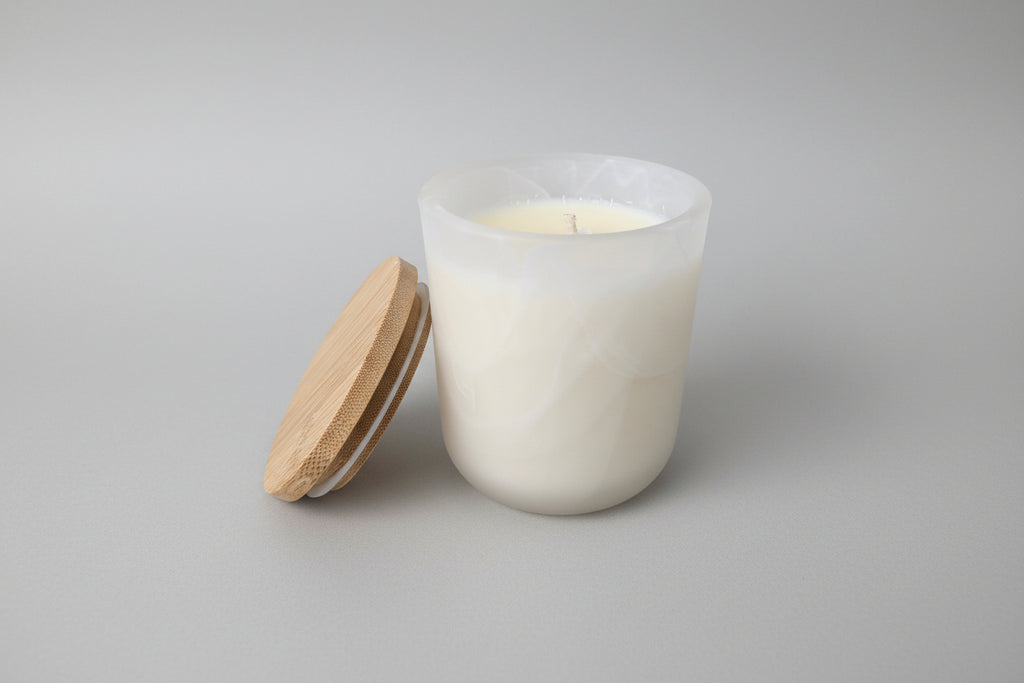 White candle in a glass jar with a wooden lid on a light surface