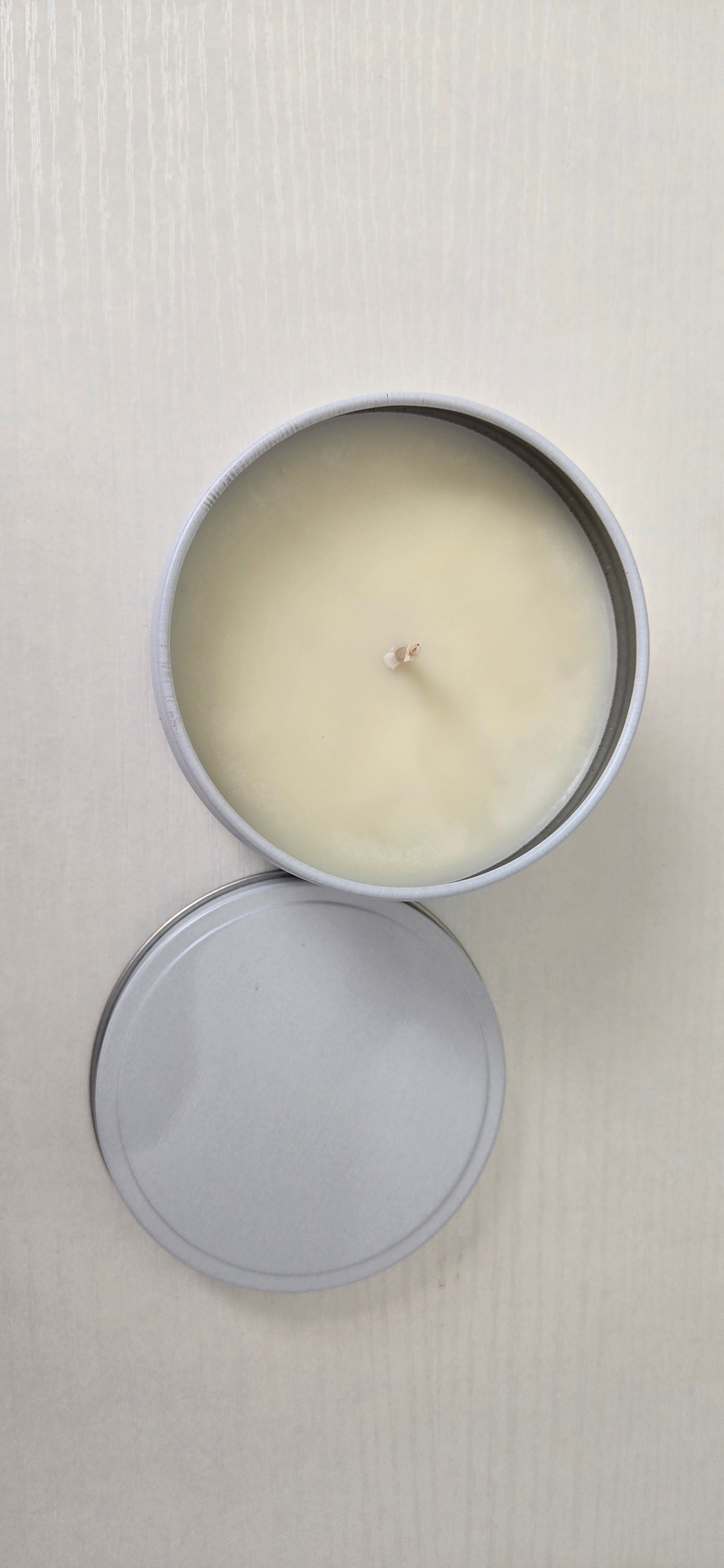 Candle in a metal tin with lid on a light gray background