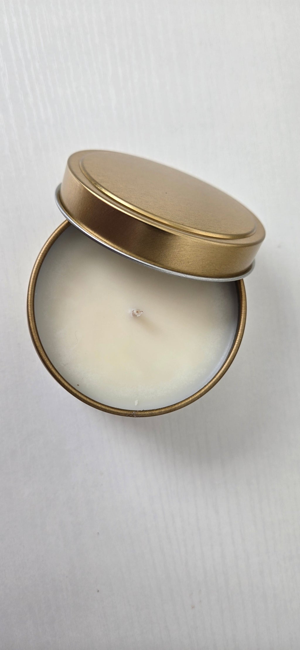 Candle in a round tin with a gold lid on a white background